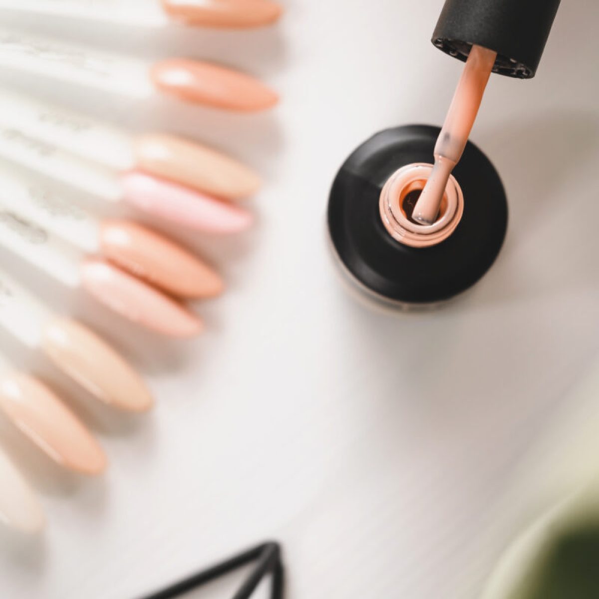 Gel lacquer standing at table. Close up view of black bottle standing at the white table, hand holding brush at the nail salon, color samples. Beauty routine concept. Top view
