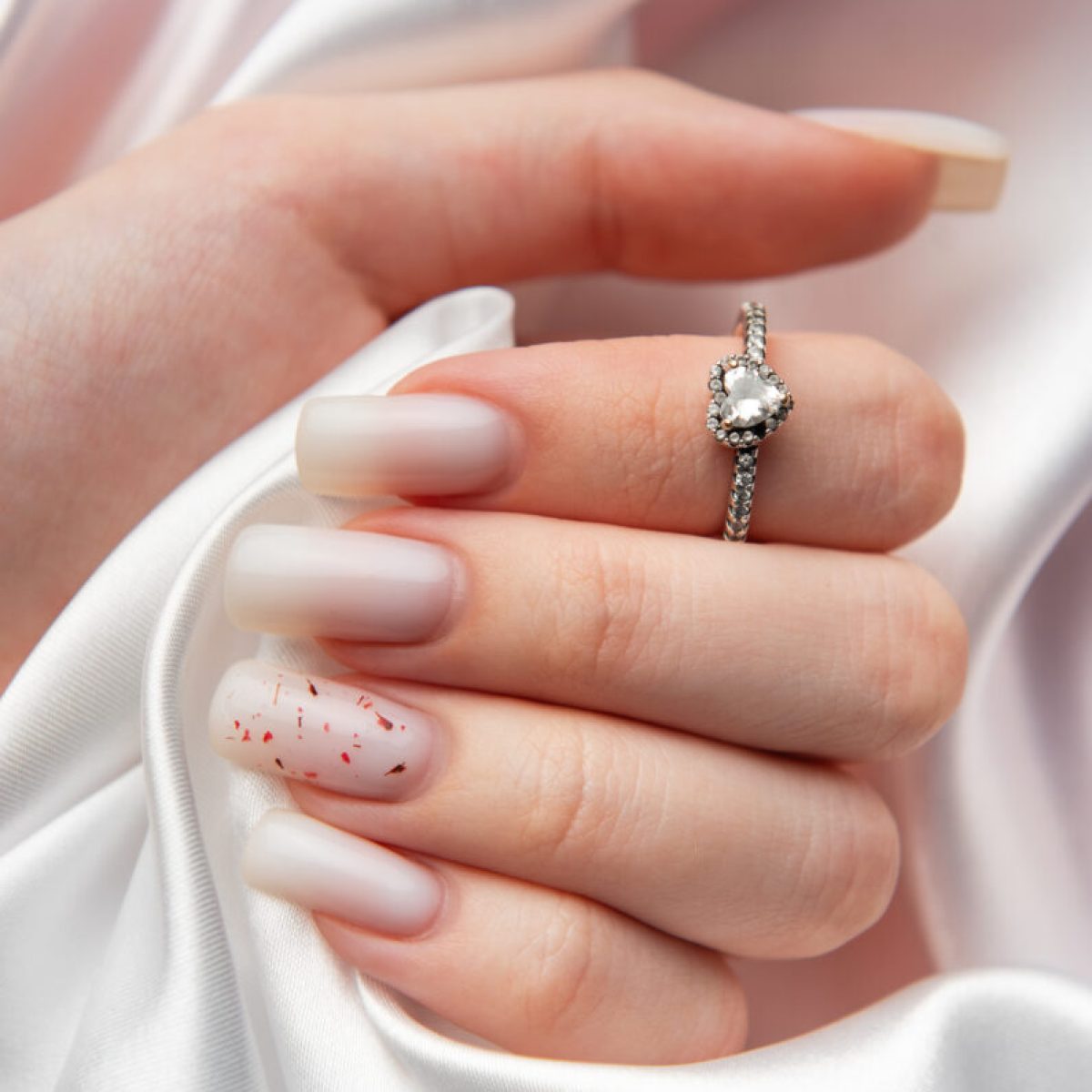 Woman showing off her new elegant diamond ring with heart shaped stone on a white silk background